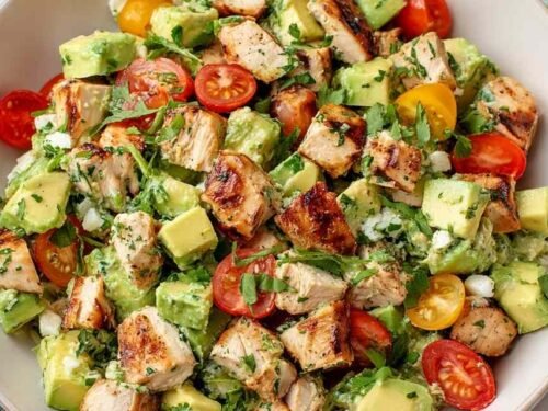 Avocado chicken salad in a large white bowl with diced avocado, cherry tomatoes, cucumber, and cilantro tossed in lime dressing