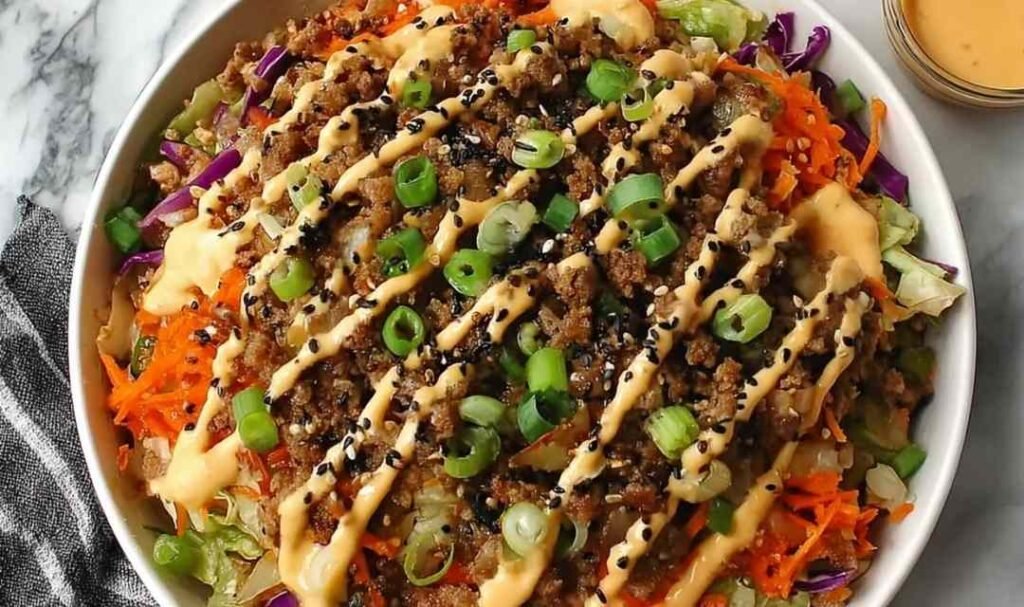 Blackstone Egg Roll in a Bowl with ground pork, shredded cabbage, carrots, sesame seeds, and spicy mayo served in a white bowl