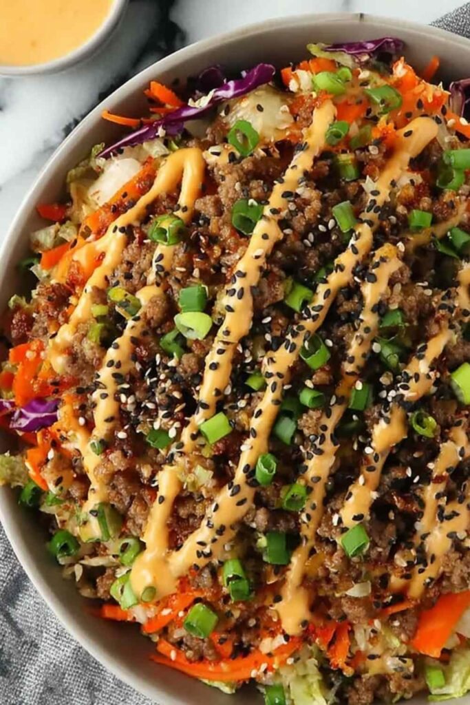 Blackstone Egg Roll in a Bowl with ground pork, shredded cabbage, carrots, sesame seeds, and spicy mayo served in a white bowl