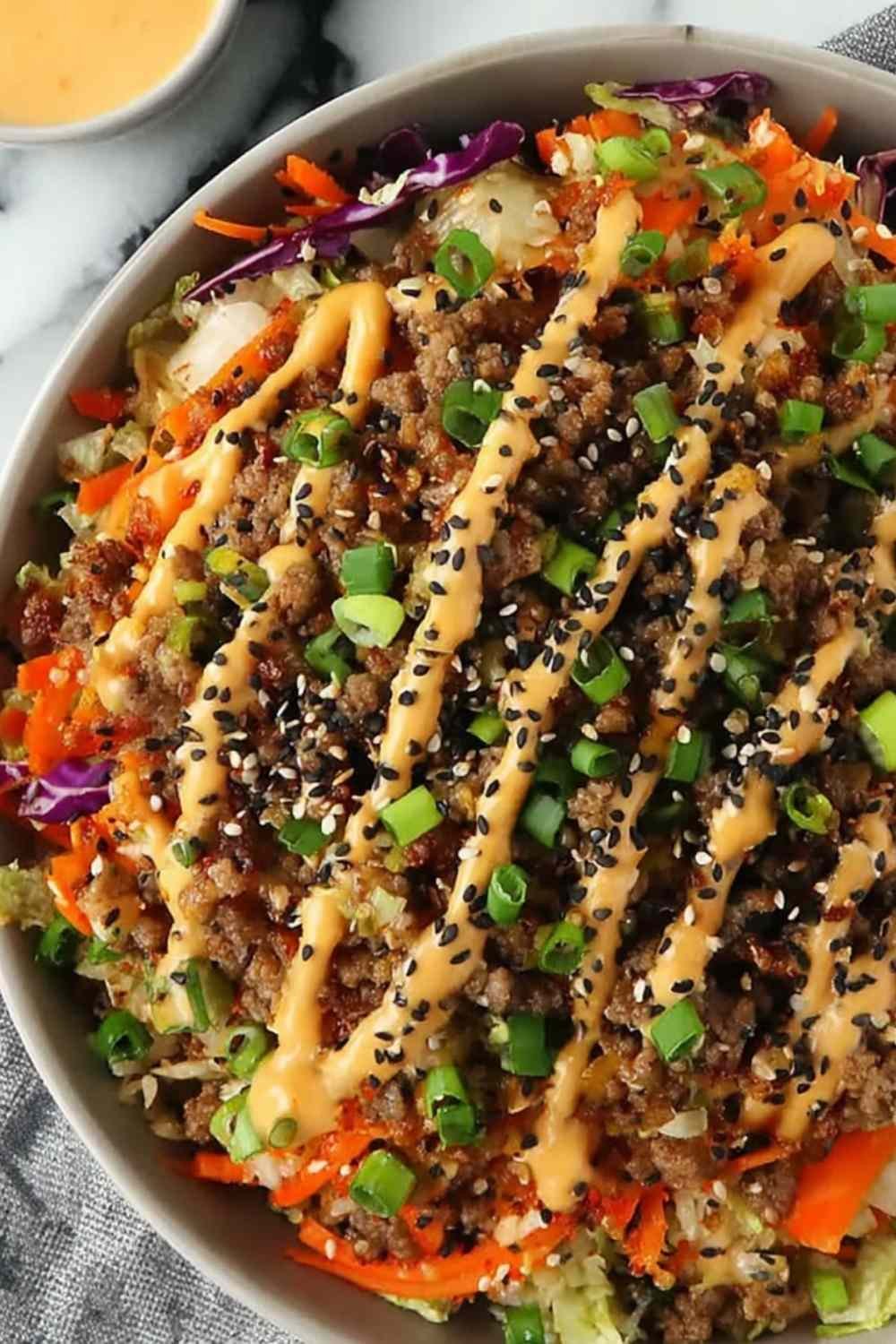 Blackstone Egg Roll in a Bowl with ground pork, shredded cabbage, carrots, sesame seeds, and spicy mayo served in a white bowl