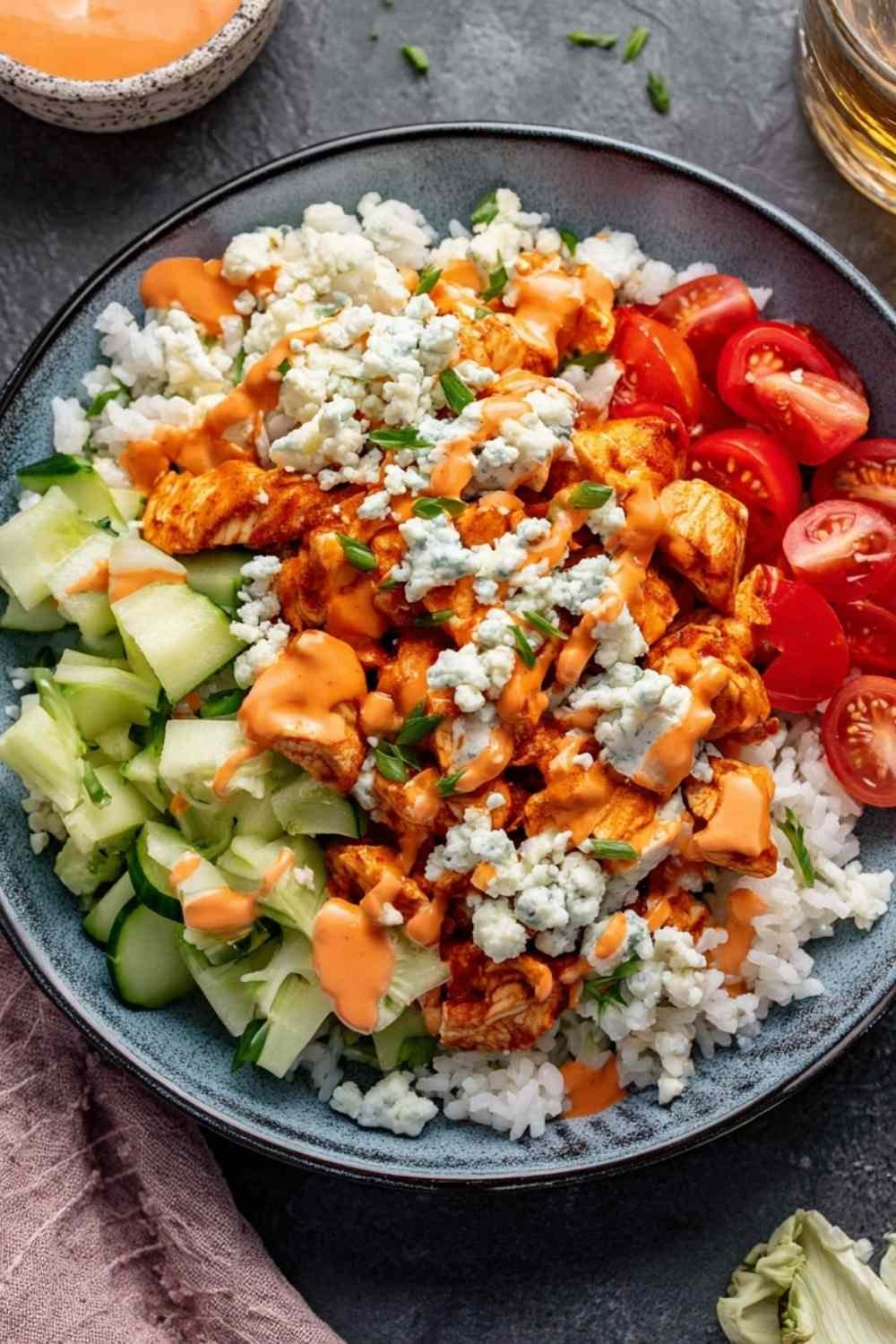 High protein buffalo chicken bowls with rice, fresh vegetables, and creamy buffalo Greek yogurt dressing