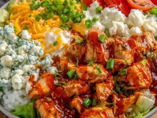 Buffalo chicken protein bowl with spicy sauced chicken over white rice topped with shredded lettuce, cherry tomatoes, cheddar cheese, and ranch drizzle