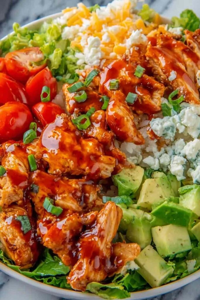 Buffalo chicken protein bowl with spicy sauced chicken over white rice topped with shredded lettuce, cherry tomatoes, cheddar cheese, and ranch drizzle