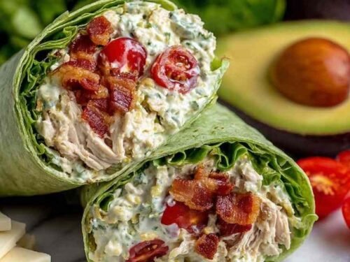 California club wraps sliced in half on a plate showing layers of chicken, avocado, bacon, and Monterey Jack cheese
