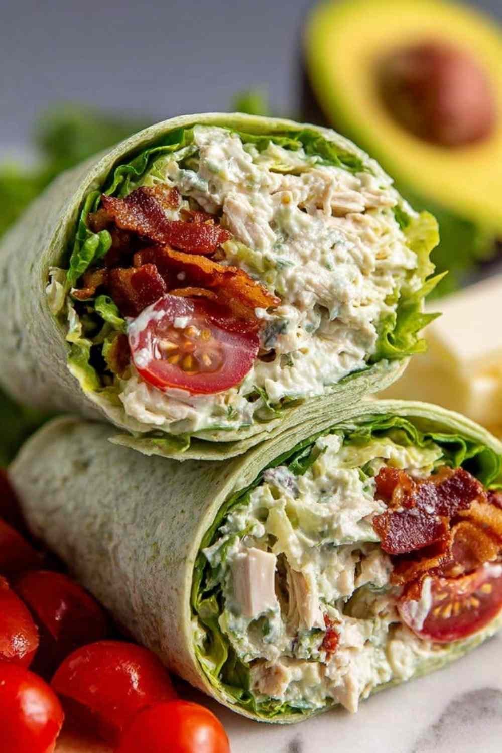 California club wraps sliced in half on a plate showing layers of chicken, avocado, bacon, and Monterey Jack cheese