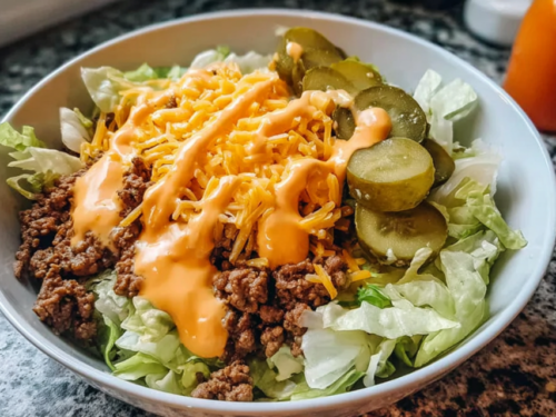 Close-up of a cheeseburger bowl with seasoned ground beef, shredded cheddar, pickles, and tangy sauce over crisp lettuce