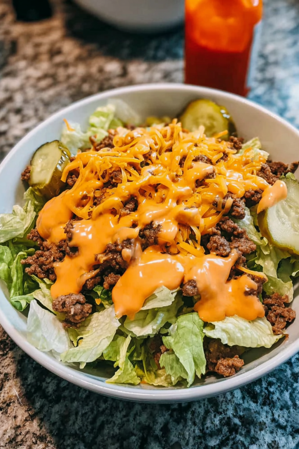 Close-up of a cheeseburger bowl with seasoned ground beef, shredded cheddar, pickles, and tangy sauce over crisp lettuce