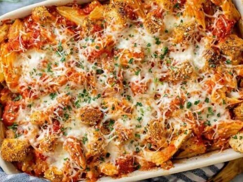 Chicken Parmesan casserole in a white baking dish with melted mozzarella, crispy chicken, and fresh parsley garnish