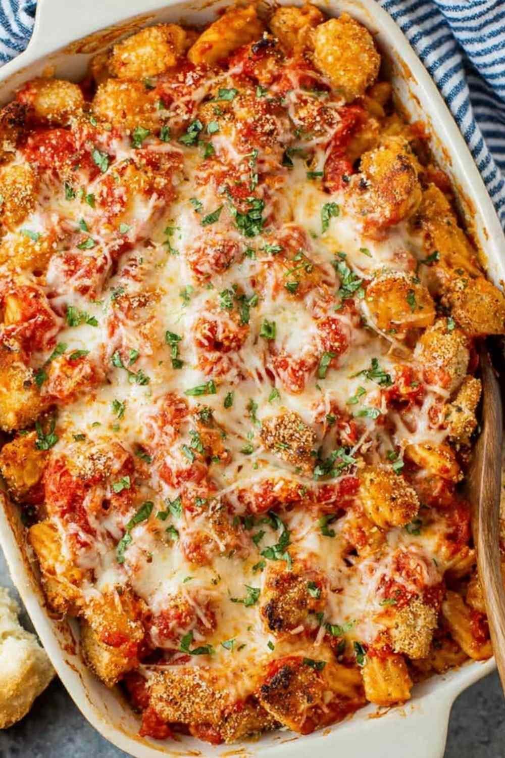Chicken Parmesan casserole in a white baking dish with melted mozzarella, crispy chicken, and fresh parsley garnish