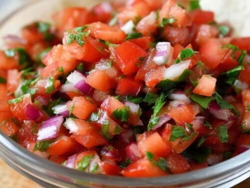 Bowl of copycat Chipotle pico de gallo with diced tomatoes, white onion, cilantro, and jalapeño with lime wedge on the side
