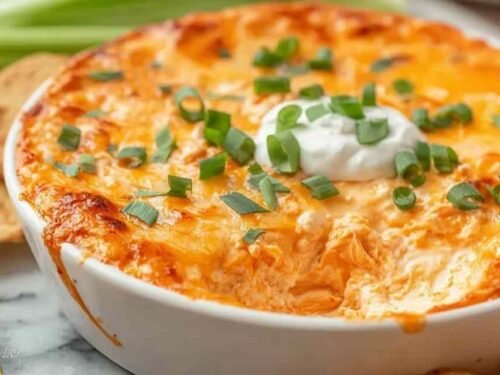 Cottage cheese buffalo chicken dip in a white baking dish with golden bubbling edges, buffalo sauce drizzle, and chopped green onions on top