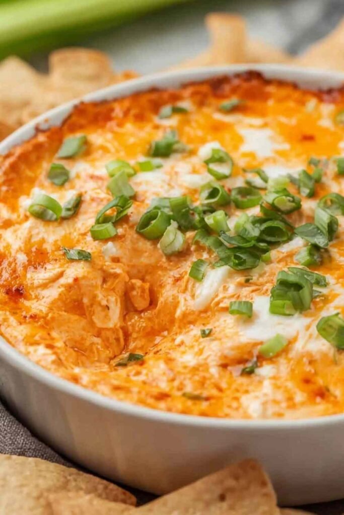 Cottage cheese buffalo chicken dip in a white baking dish with golden bubbling edges, buffalo sauce drizzle, and chopped green onions on top