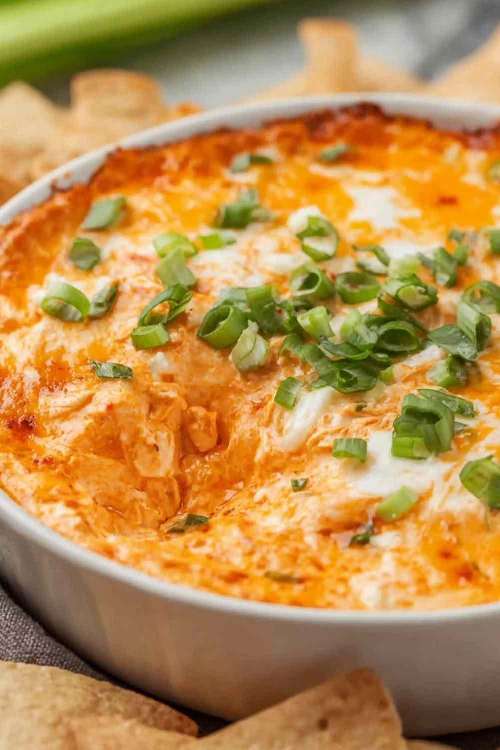 Cottage cheese buffalo chicken dip in a white baking dish with golden bubbling edges, buffalo sauce drizzle, and chopped green onions on top