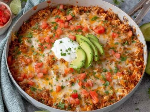 One pot taco skillet with ground beef, melted cheddar, and sliced avocado garnish in a large saute pan