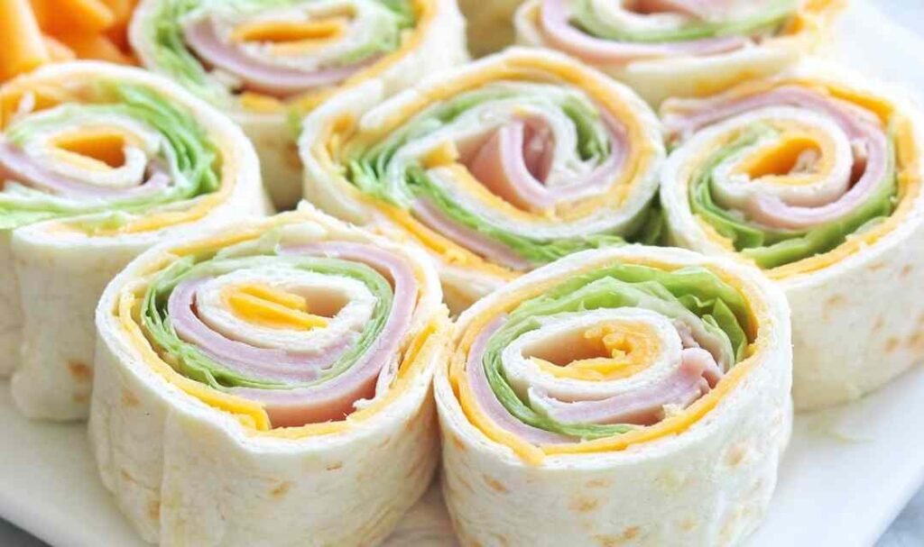 Turkey roll ups with cheddar and cream cheese sliced into rounds on a wooden cutting board