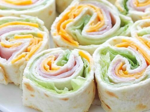 Turkey roll ups with cheddar and cream cheese sliced into rounds on a wooden cutting board