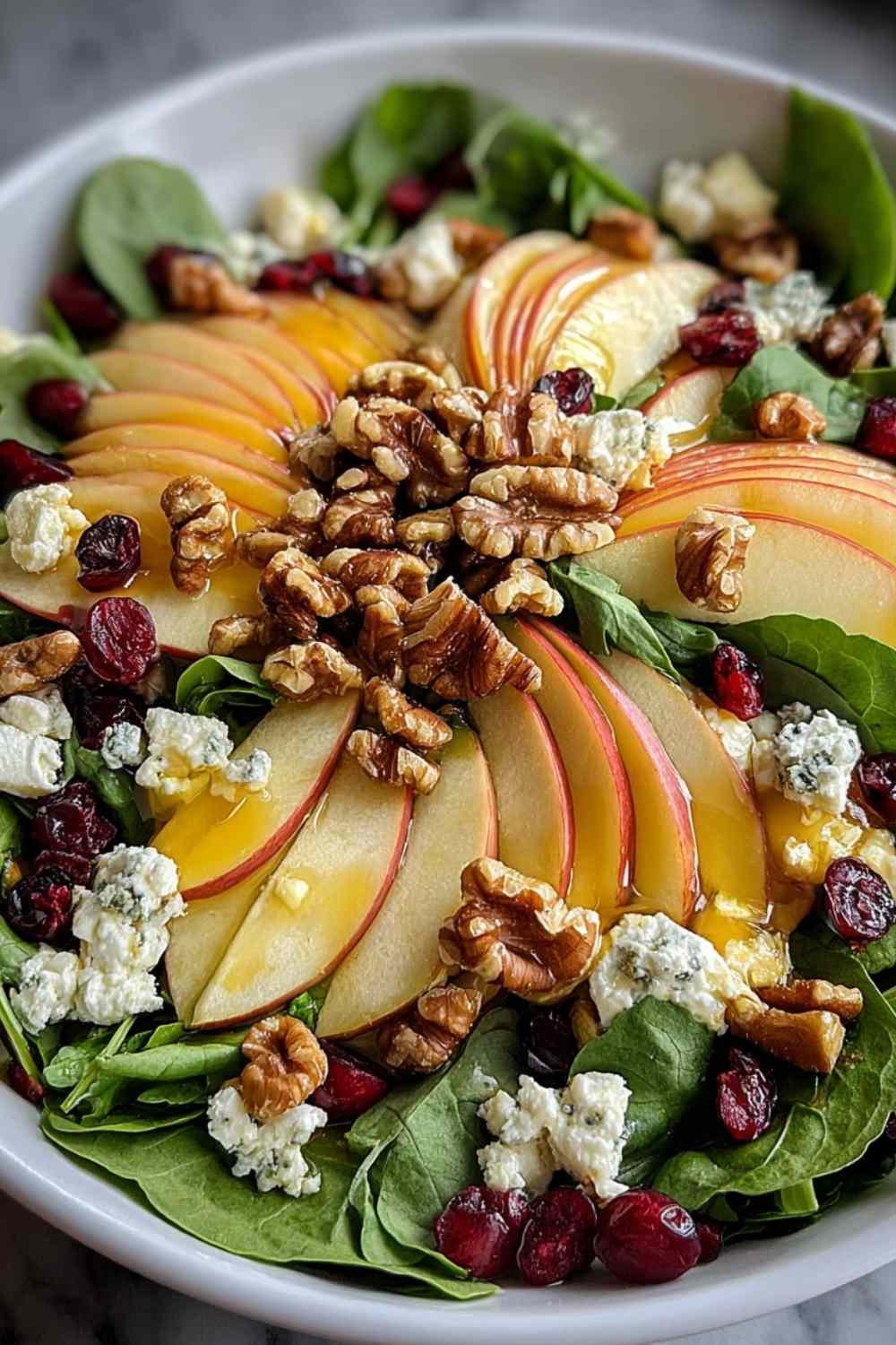 Fresh walnut apple salad with mixed greens cranberries and goat cheese in white bowl