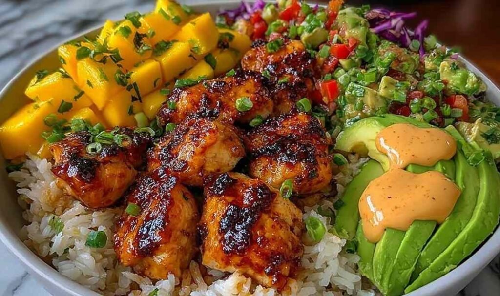 Grilled maple sriracha chicken bites bowl with coconut rice, mango avocado salsa, and chili mayo drizzle in a white bowl