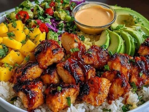 Grilled maple sriracha chicken bites bowl with coconut rice, mango avocado salsa, and chili mayo drizzle in a white bowl