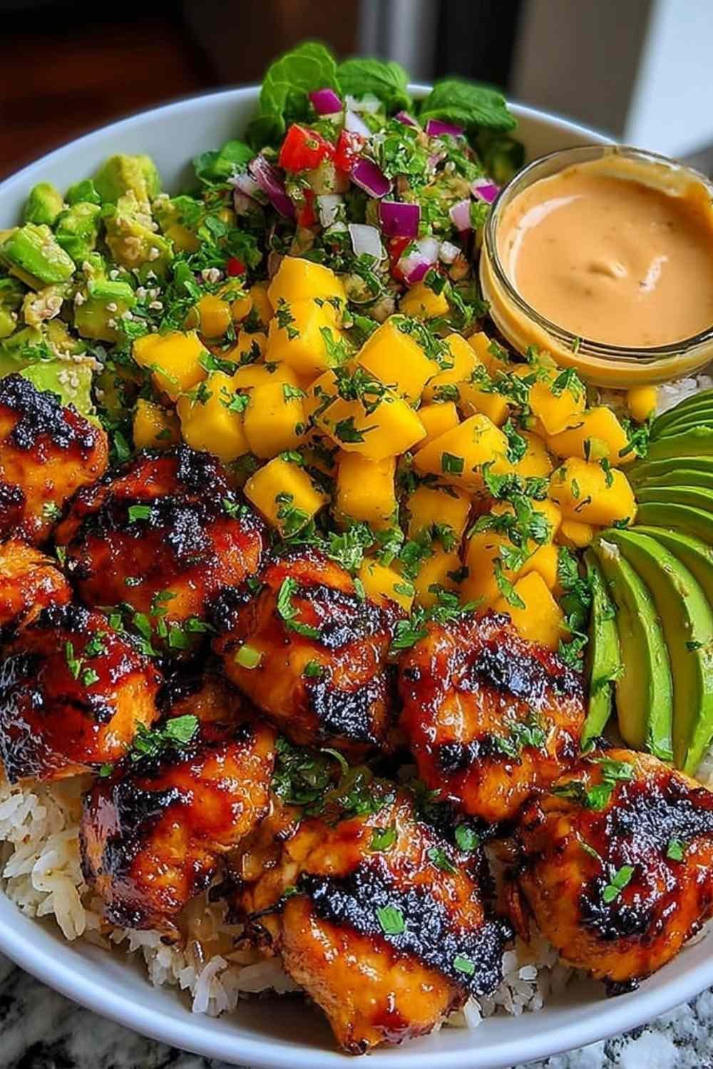Grilled maple sriracha chicken bites bowl with coconut rice, mango avocado salsa, and chili mayo drizzle in a white bowl