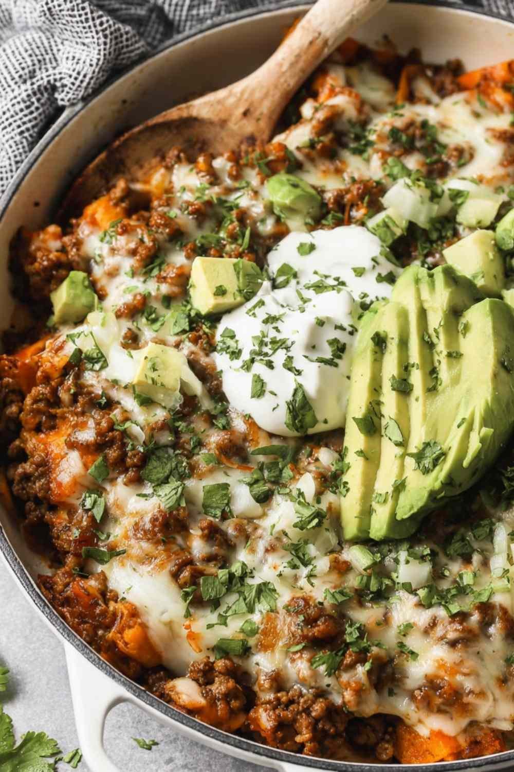 Ground Beef Enchilada Skillet in a large pan topped with sliced avocado, fresh cilantro, and dairy-free sour cream ready to serve