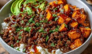 Ground beef hot honey bowl with roasted sweet potatoes, cottage cheese, sliced avocado, and hot honey drizzle in a white bowl