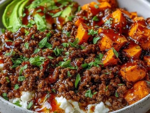 Ground beef hot honey bowl with roasted sweet potatoes, cottage cheese, sliced avocado, and hot honey drizzle in a white bowl