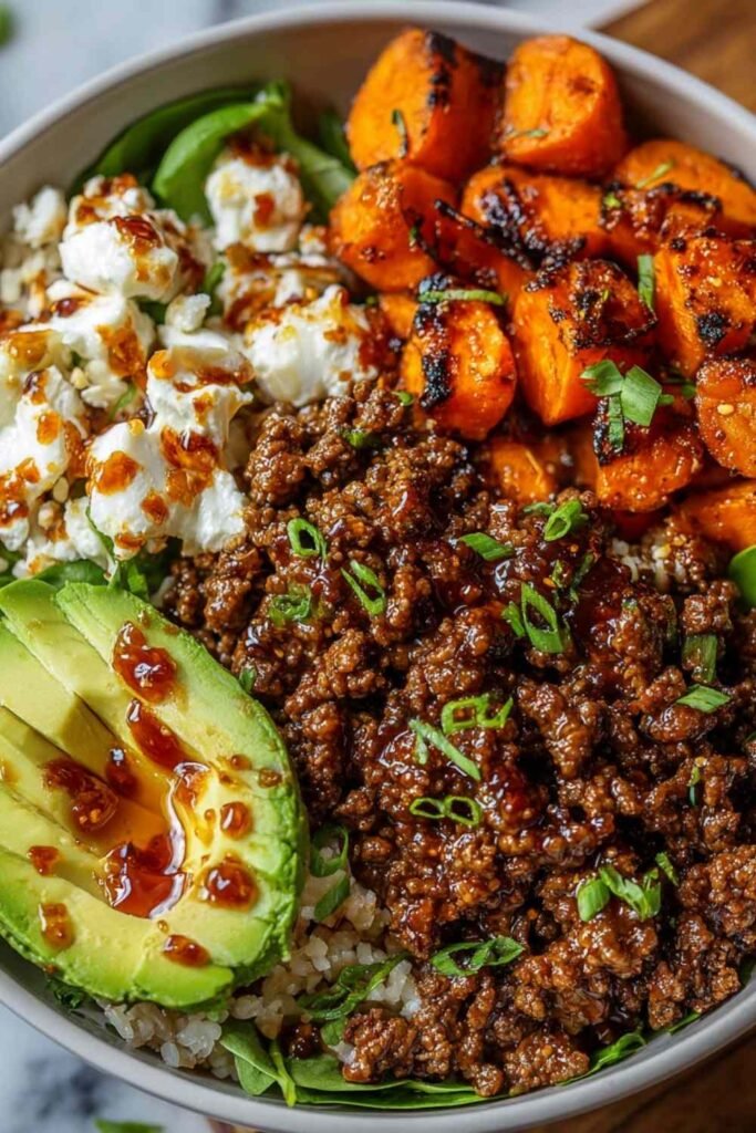Ground beef hot honey bowl with roasted sweet potatoes, cottage cheese, sliced avocado, and hot honey drizzle in a white bowl