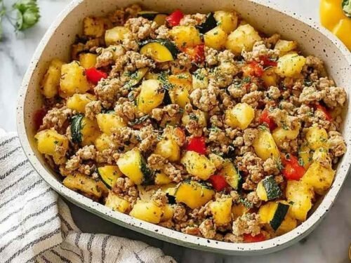 Ground turkey hash with zucchini, bell peppers, yellow squash, and a runny fried egg garnished with fresh parsley