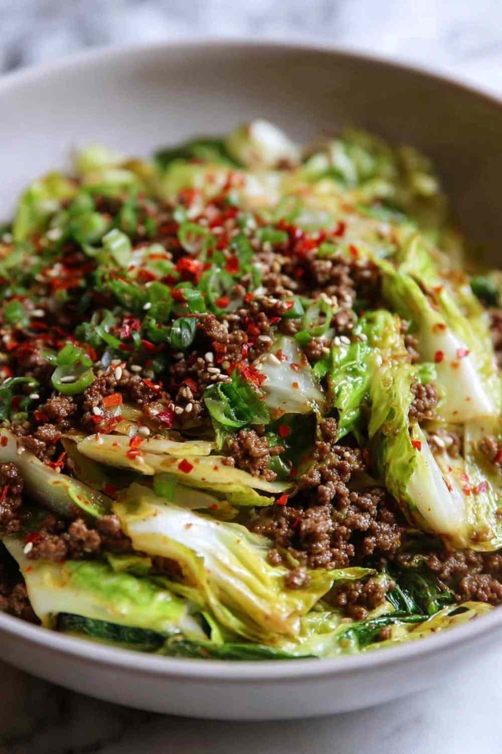 Chinese ground beef cabbage stir fry with sesame seeds and green onions served in a large skillet