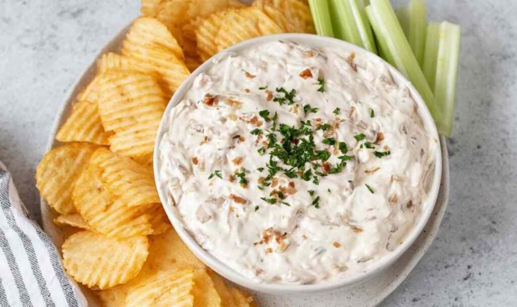 Healthy onion dip made with caramelized onions and Greek yogurt served in a white bowl with kettle chips and fresh vegetables