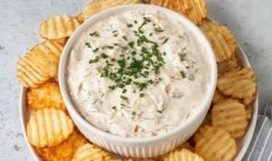 Healthy onion dip made with caramelized onions and Greek yogurt served in a white bowl with kettle chips and fresh vegetables