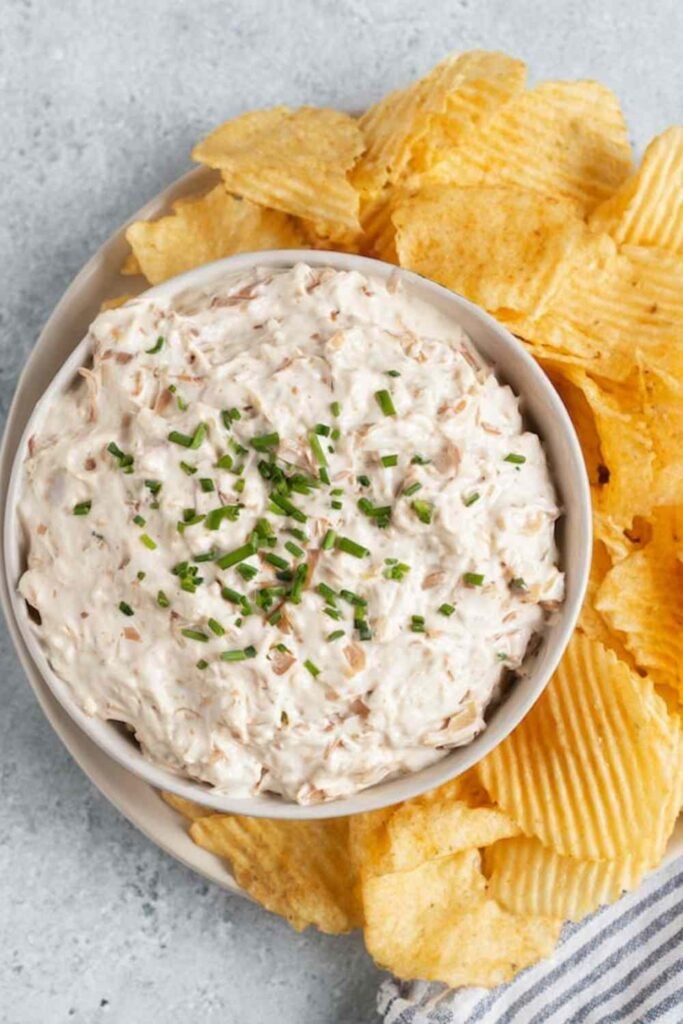 Healthy onion dip made with caramelized onions and Greek yogurt served in a white bowl with kettle chips and fresh vegetables