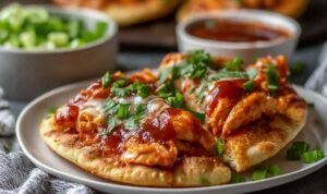 Four high-protein BBQ chicken flatbreads on a baking sheet with golden melted cheese, shredded chicken in BBQ sauce, red onion, and fresh cilantro