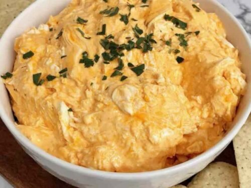 High protein buffalo chicken dip in a white bowl garnished with green onions and blue cheese crumbles served with celery and tortilla chips