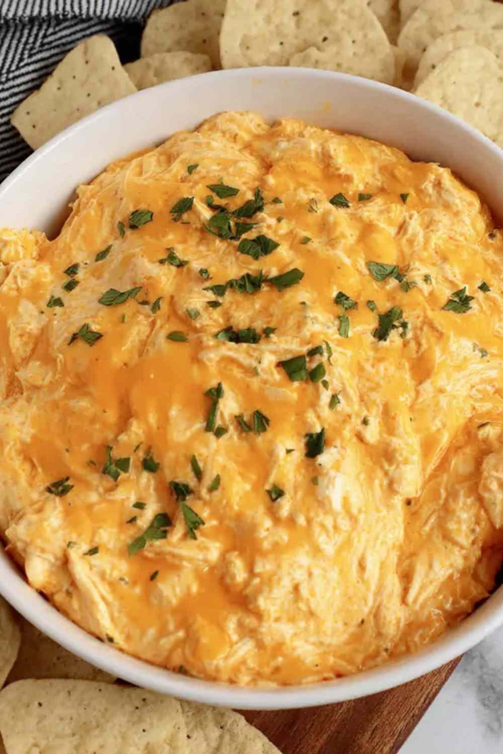 High protein buffalo chicken dip in a white bowl garnished with green onions and blue cheese crumbles served with celery and tortilla chips