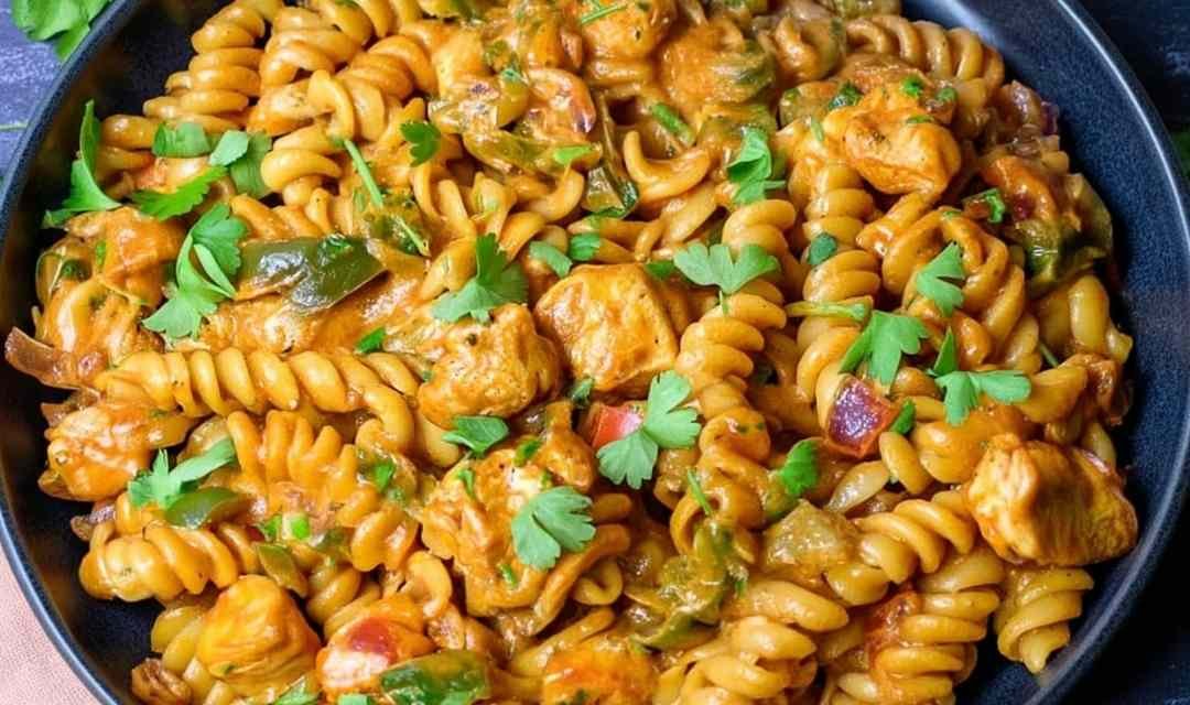 High protein chicken fajita pasta in a large skillet with creamy cheddar sauce, golden chicken pieces, and diced bell peppers