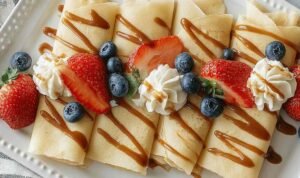 High protein egg white crepes stacked on white plate with fresh berries and honey drizzle