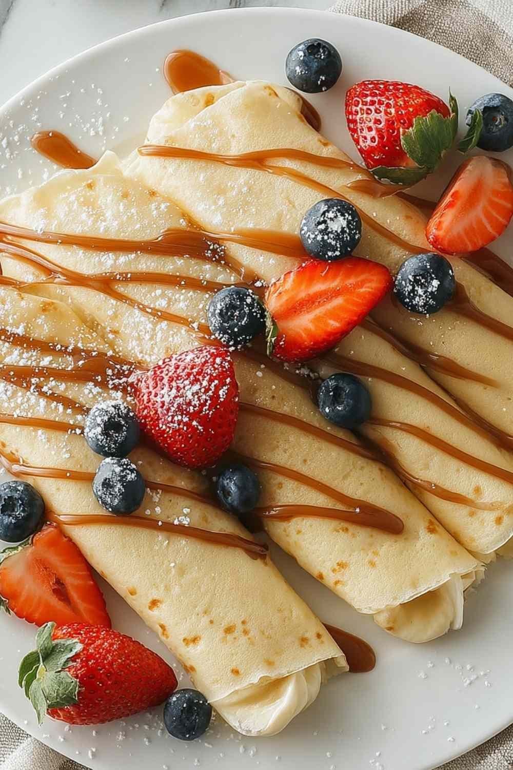 High protein egg white crepes stacked on white plate with fresh berries and honey drizzle
