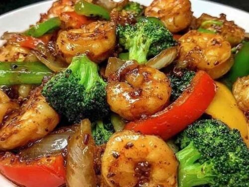 High-protein shrimp stir fry with noodles, broccoli, snap peas, and bell pepper in a glossy garlic-soy sauce served in a wok