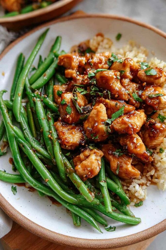 Honey garlic chicken and green beans in a skillet with glossy sweet savory sauce sesame seeds and green onions