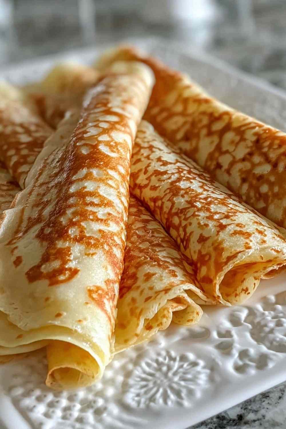 Stack of golden oatmeal crepes on a white plate topped with fresh berries and a drizzle of maple syrup