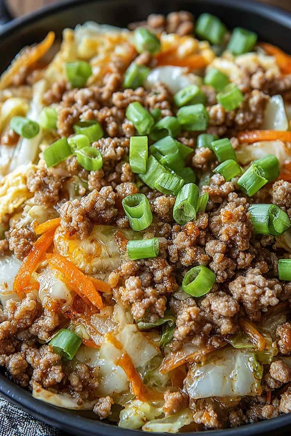 Keto egg roll in a bowl in a large skillet with shredded cabbage, ground pork, carrots, and green onions