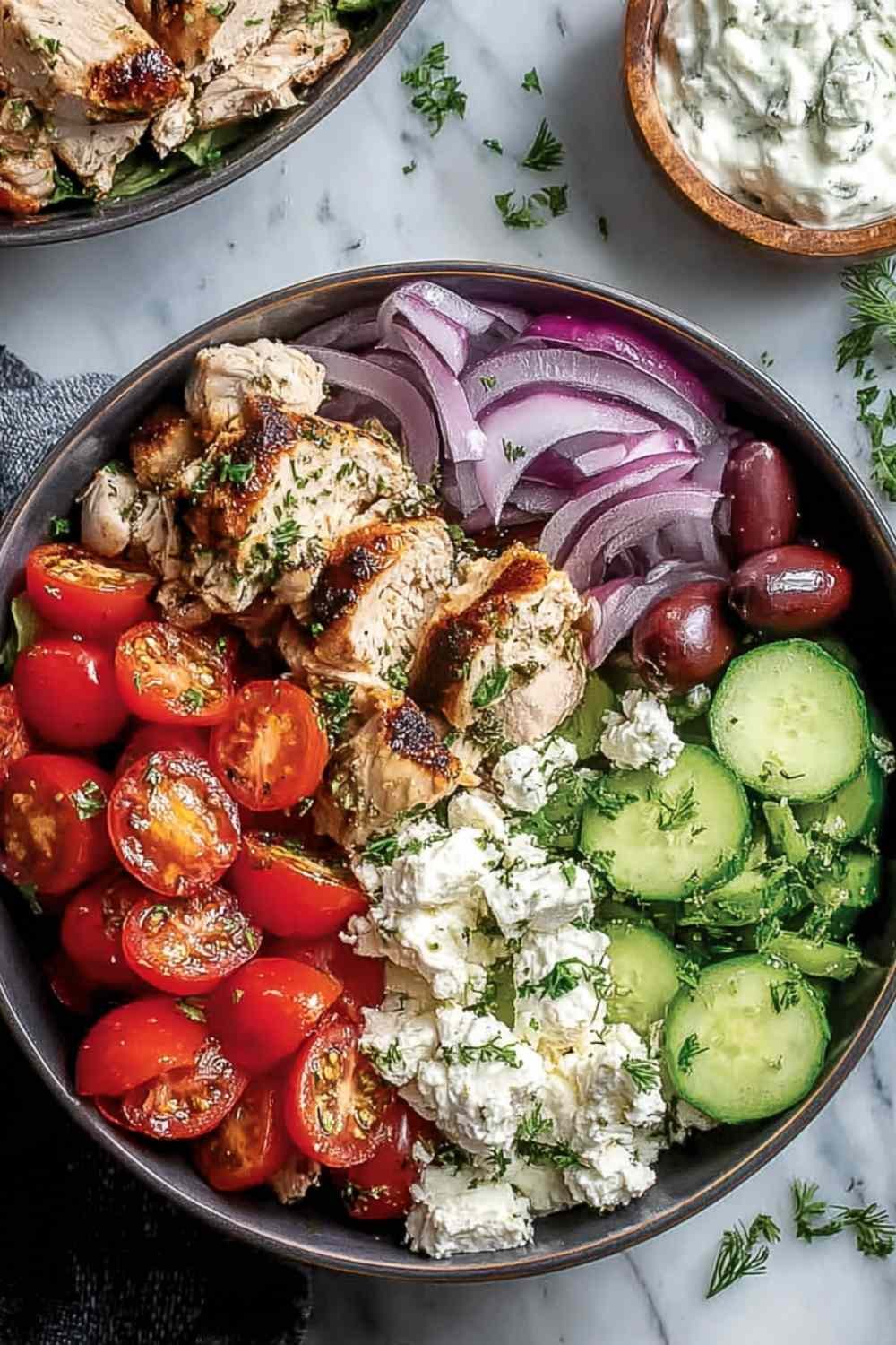 Low-carb Greek chicken bowls with sliced marinated chicken, homemade tzatziki, crumbled feta, cherry tomatoes, and Kalamata olives