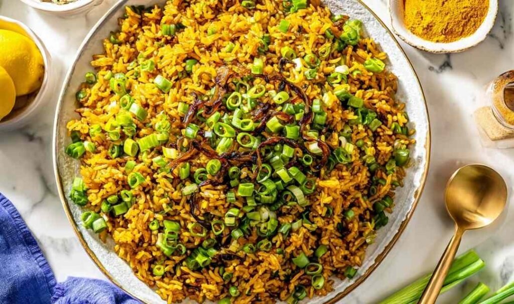 Mujadara lentils and rice on a serving platter topped with caramelized onions, fresh parsley, and lemon wedges