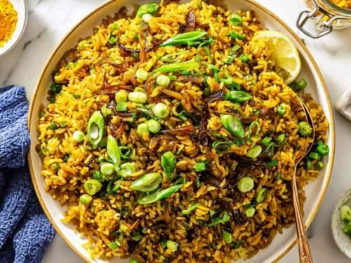Mujadara lentils and rice on a serving platter topped with caramelized onions, fresh parsley, and lemon wedges