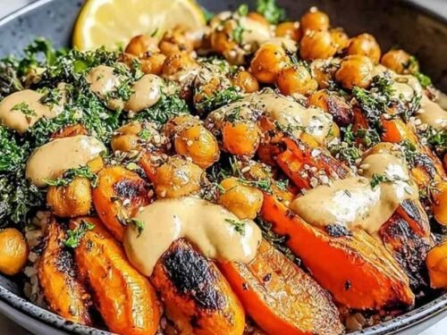 Roasted carrot and chickpea bowl served over quinoa with creamy tahini dressing drizzled on top and fresh herbs garnish