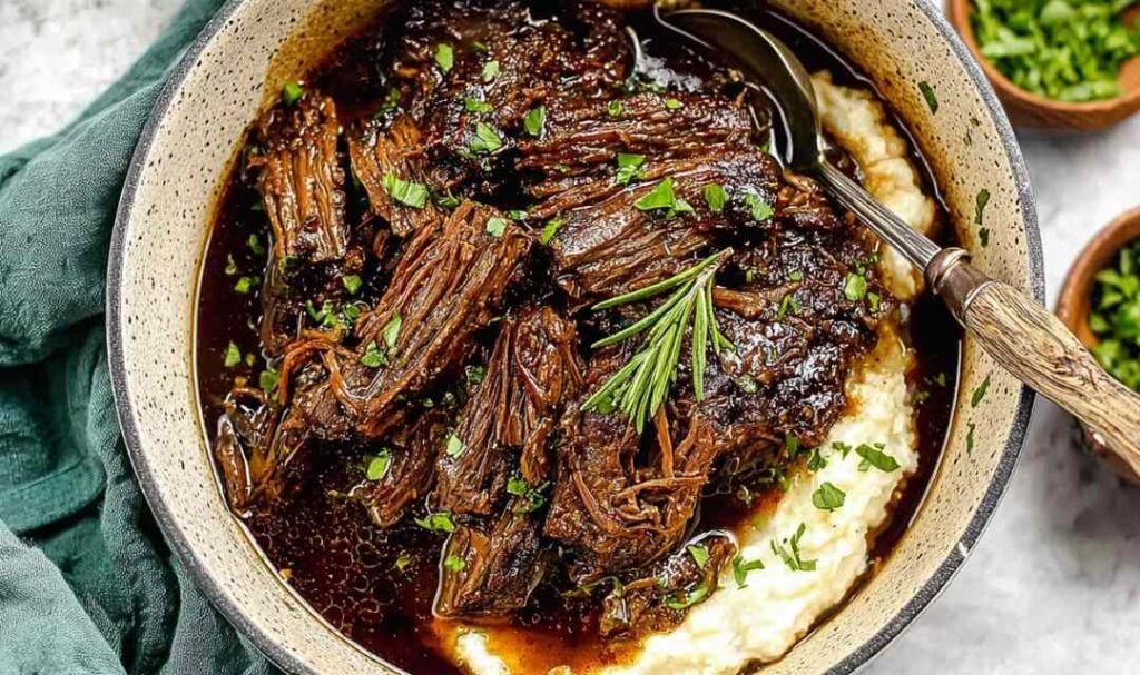 Oven braised beef chuck roast shredded in braising liquid with carrots and herbs