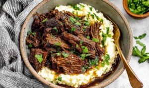 Oven braised beef chuck roast shredded in braising liquid with carrots and herbs