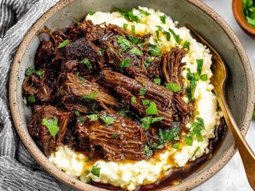 Oven braised beef chuck roast shredded in braising liquid with carrots and herbs